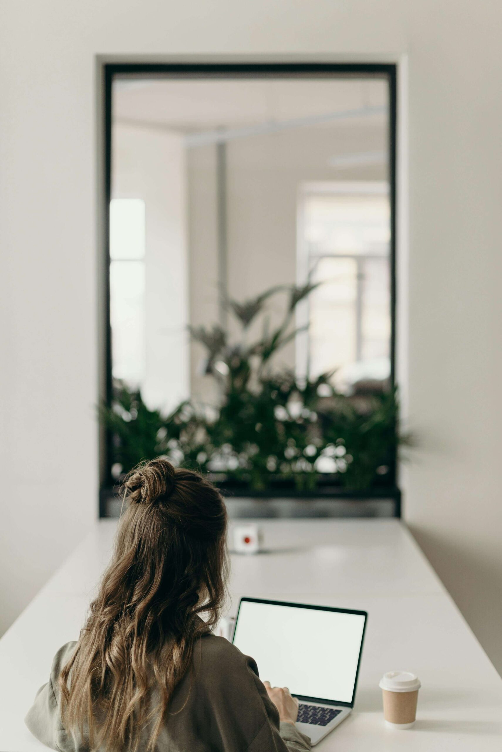 Woman typing on a laptop at a table in front of a mirror
