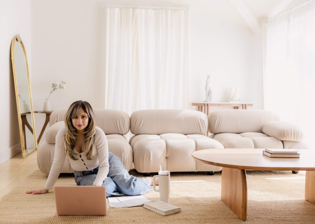 Founder of Designed by Harj sitting on the floor working on a laptop in her Soft Girl CEO era